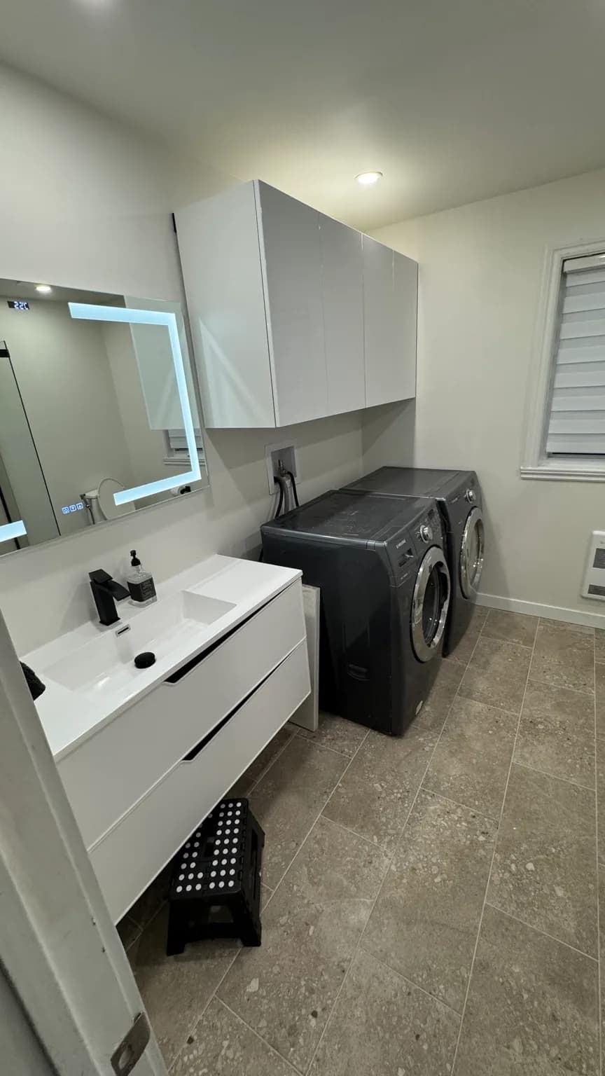 Salle d’eau rénovée à Pierrefonds-Roxboro avec douche vitrée, vanité murale et zone buanderie.